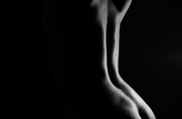 Photographie monochrome d'une femme nue gracieuse dévoilant son dos et ses fesses