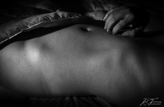 Low-key fine art photography of woman hiding her nude body under the blanket